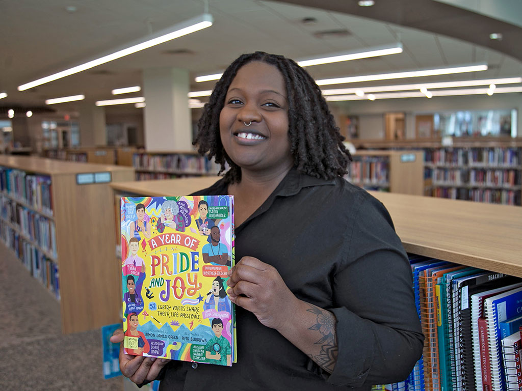 Associate Professor Myeshia Price holding the book "A Year of Pride and Joy: LGBTQ+ Voices Share Their Life Passions."